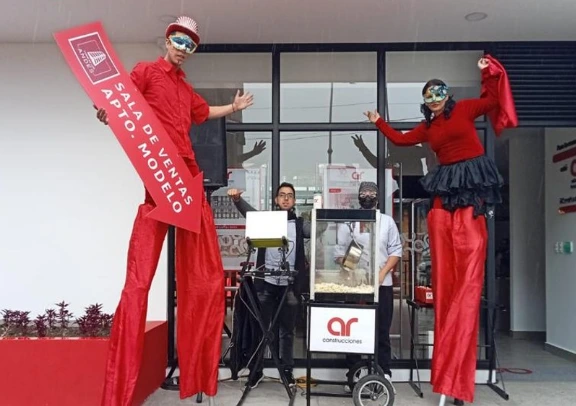 Activación de marca de AR Construcciones con personajes en zancos, crispetera y branding visual para atraer al público a la sala de ventas.